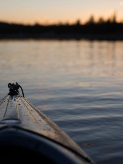 Close-up of a kayak bow on calm water during sunset.
