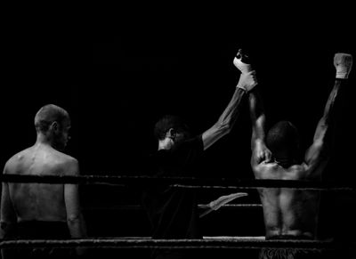 A black and white image of the winner of a boxing bout being announced by the referee