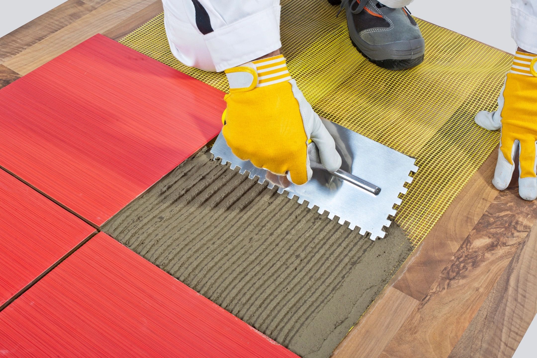 Worker spreading adhesive for red tile installation on wooden floor.
