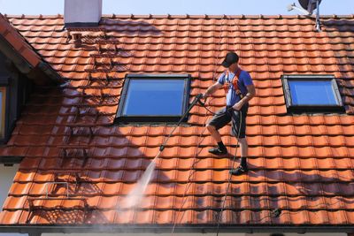 Man washing a tile roof while wearing a harness.