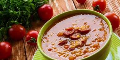 A bowl of tomato-based soup with herbs on a wooden table.