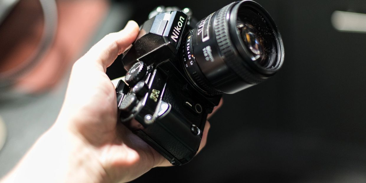 Hand holding a classic Nikon film camera with a large lens.