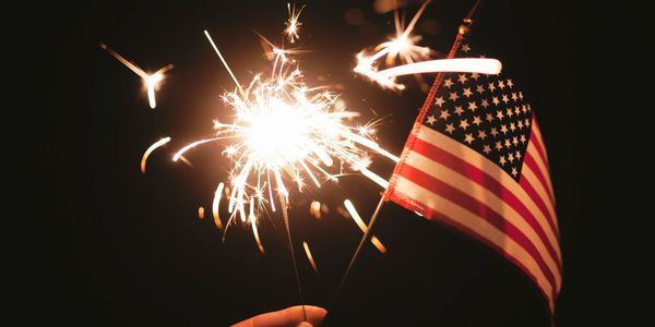 Hand holding a sparkler and a small American flag against a dark background.