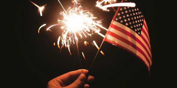 Hand holding a sparkler and a small American flag against a dark background.