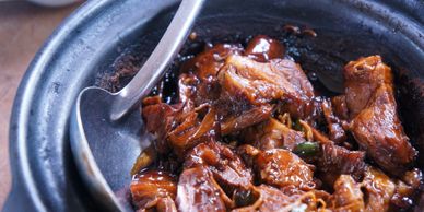 Close-up of a rich, dark-braised meat dish in a clay pot.