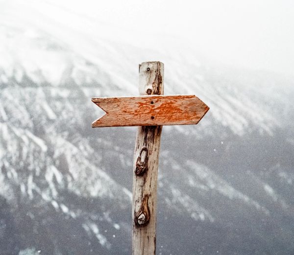 A rustic wooden signpost pointing right in a mountainous area.