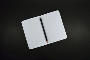 Open blank notebook with a black pencil on a dark surface.