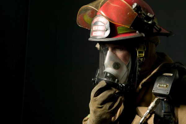 Firefighter wearing protective gear and breathing mask in a dark setting.