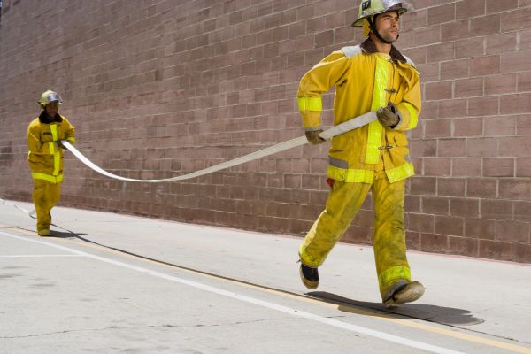 Two firefighters in yellow gear carrying a fire hose.