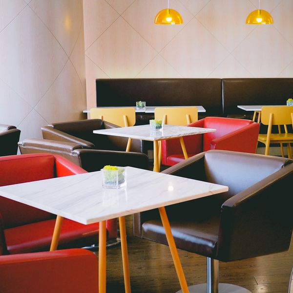 Modern cafe seating with red, brown, and yellow chairs around white tables.