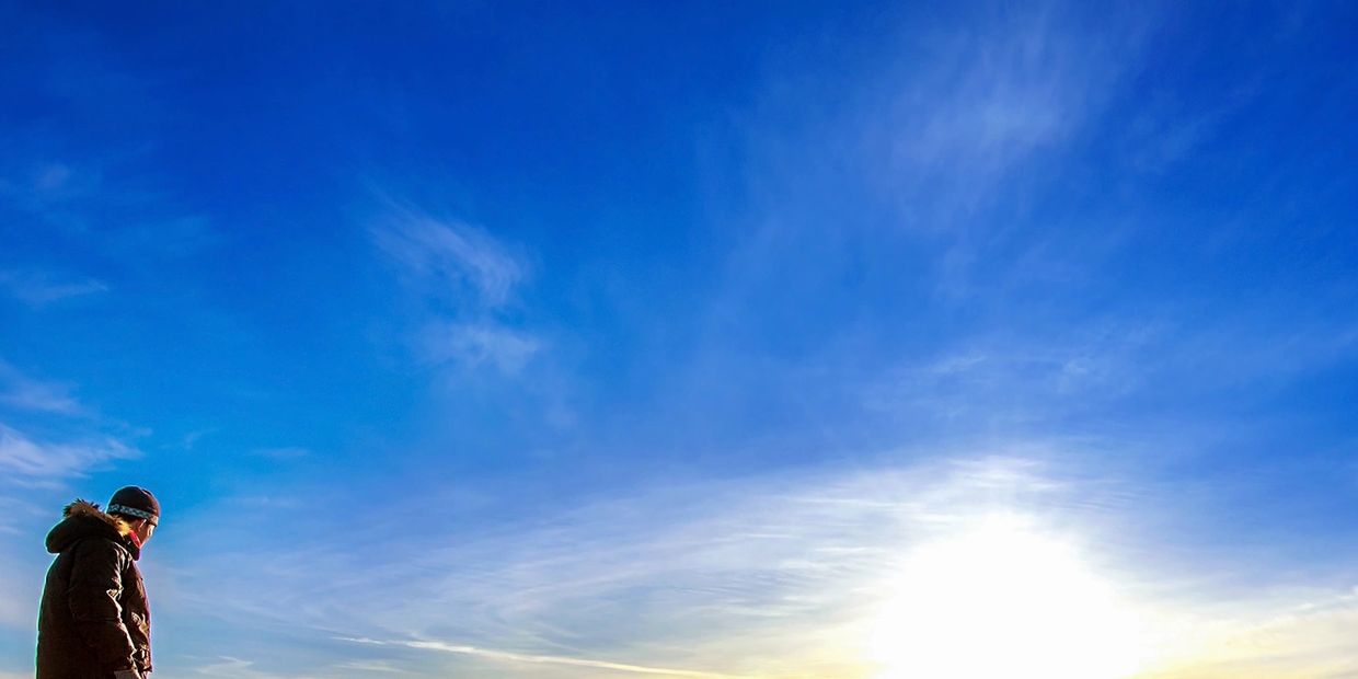 Person looking at a bright sunrise under a vast blue sky.