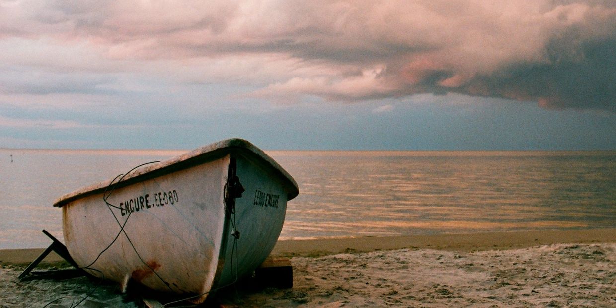 A boat on the sandy shore with a cloudy sky and calm sea.