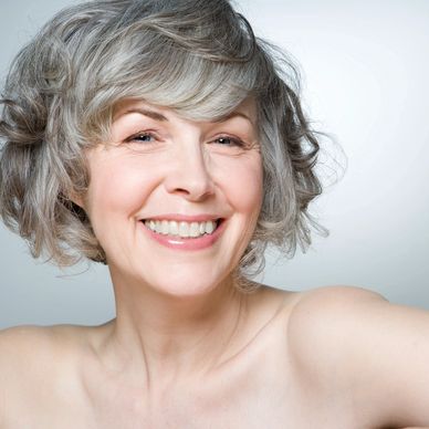 woman with short grey hair and bare shoulders, smiling at the camera