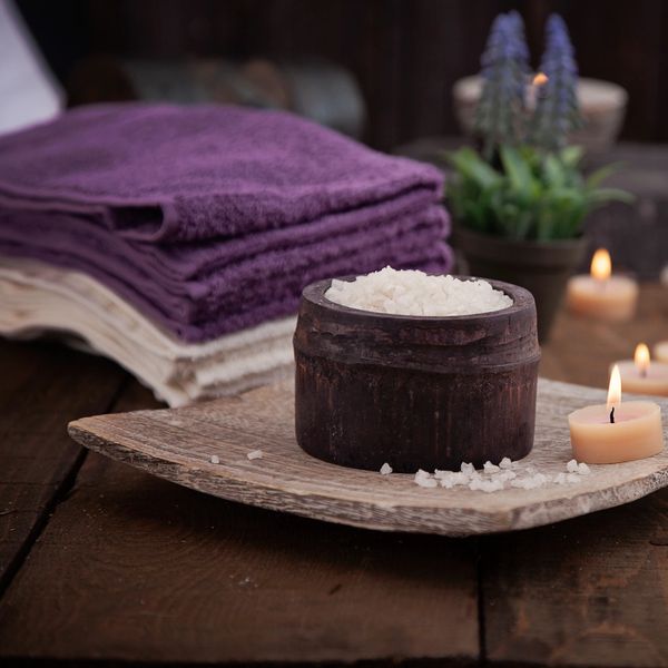 Spa setup with sea salt, candles, and towels on a wooden tray.