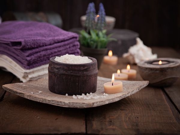 Candles burning next to lavender, rock salt and towels, in a relaxing reflexology treatment room.