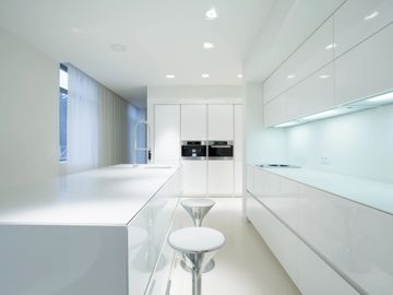 Modern all-white kitchen with sleek cabinets and stools.