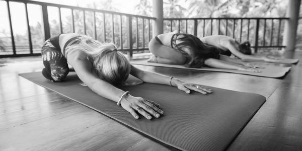 Two women practicing yoga in child’s pose on mats indoors.