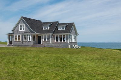 Gray home sitting on a green field with a view of the ocean. 