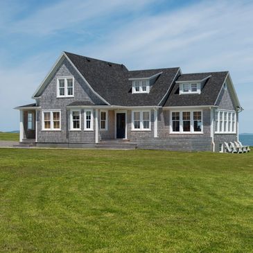 Large gray ranch style house with green grass overlooking the ocean.