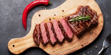 Sliced medium-rare steak garnished with rosemary on a wooden board.