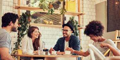Four friends laughing and enjoying coffee together at a cozy café.