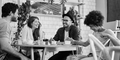 Four friends laughing and enjoying coffee together at a table.