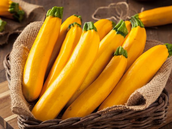A basket filled with fresh yellow zucchinis on a rustic wooden table.