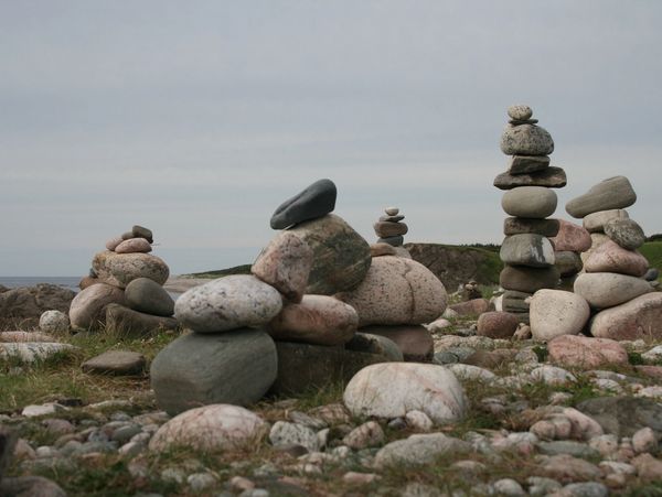 Stacks of balanced stones on a rocky landscape under a cloudy sky.