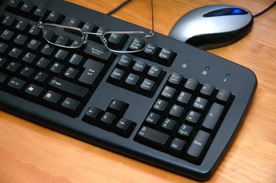 Black computer keyboard with glasses resting on it and a mouse beside.