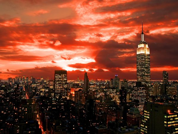 New York City skyline with a fiery sunset sky and illuminated buildings.
