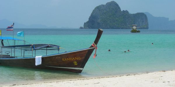 Traditional wooden boat anchored near a tropical beach with turquoise water.