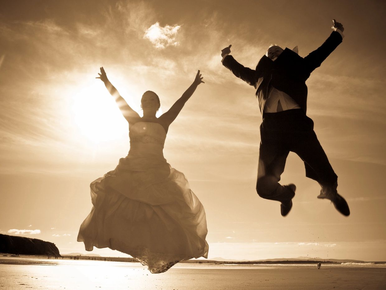 Bride and groom joyfully jumping on the beach at sunset.