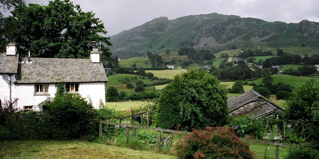 A charming white cottage in a lush green countryside with hills in the background.