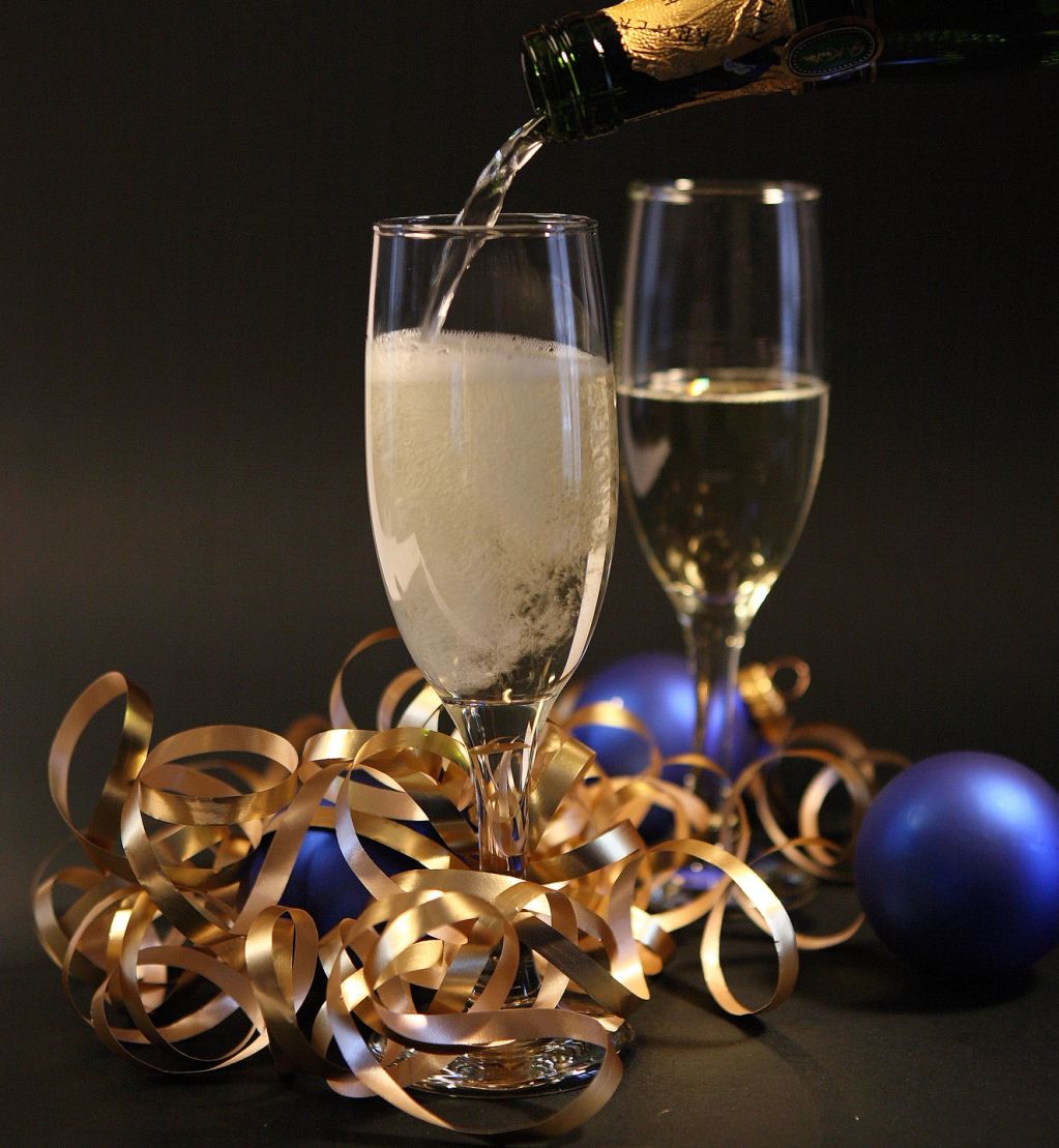 Champagne being poured into a glass surrounded by gold ribbons and blue ornaments.
