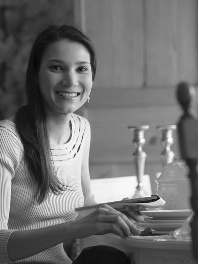 A smiling woman sitting at a table with elegant tableware and decor.
