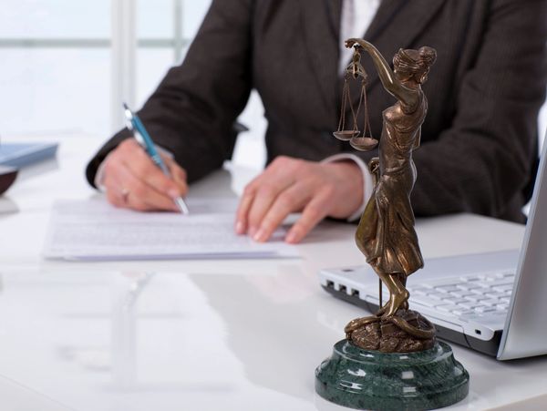 A lawyer signs documents with a Lady Justice statue in the foreground.