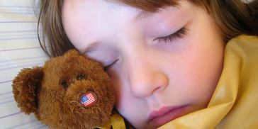 Child peacefully sleeping with a teddy bear featuring an American flag pin.