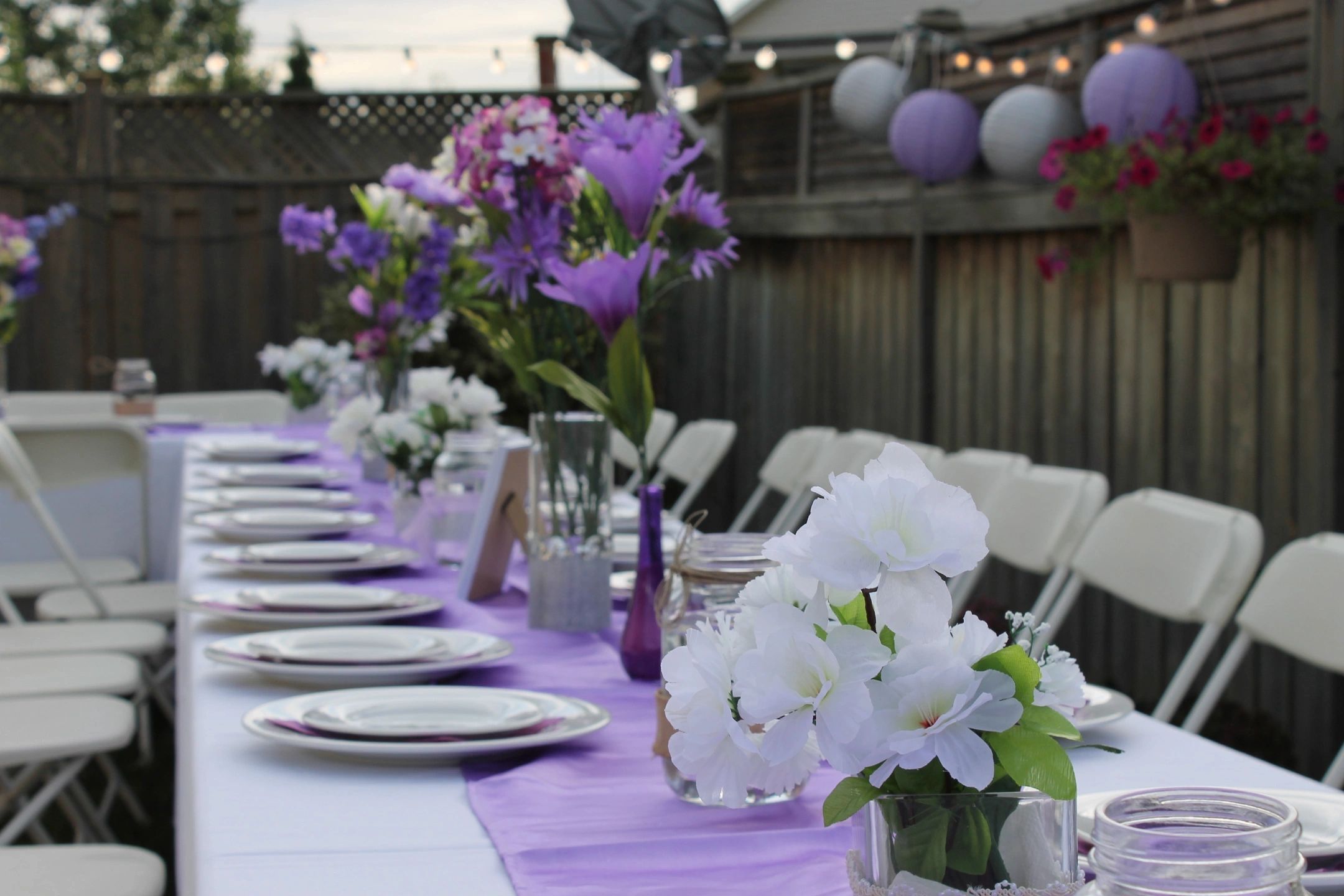 Outdoor table set with purple and white floral decorations for a celebration.