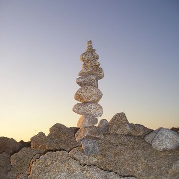 A tall stack of balanced stones on rocky terrain at sunset.