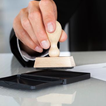 Hand holding a stamp over an ink pad next to documents.