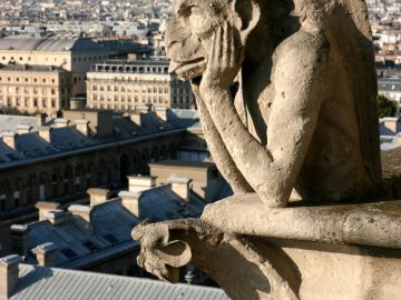 A stone gargoyle overlooking a cityscape at sunset.