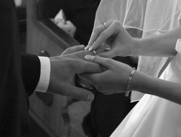 Bride putting ring on groom's finger in black and white photo.