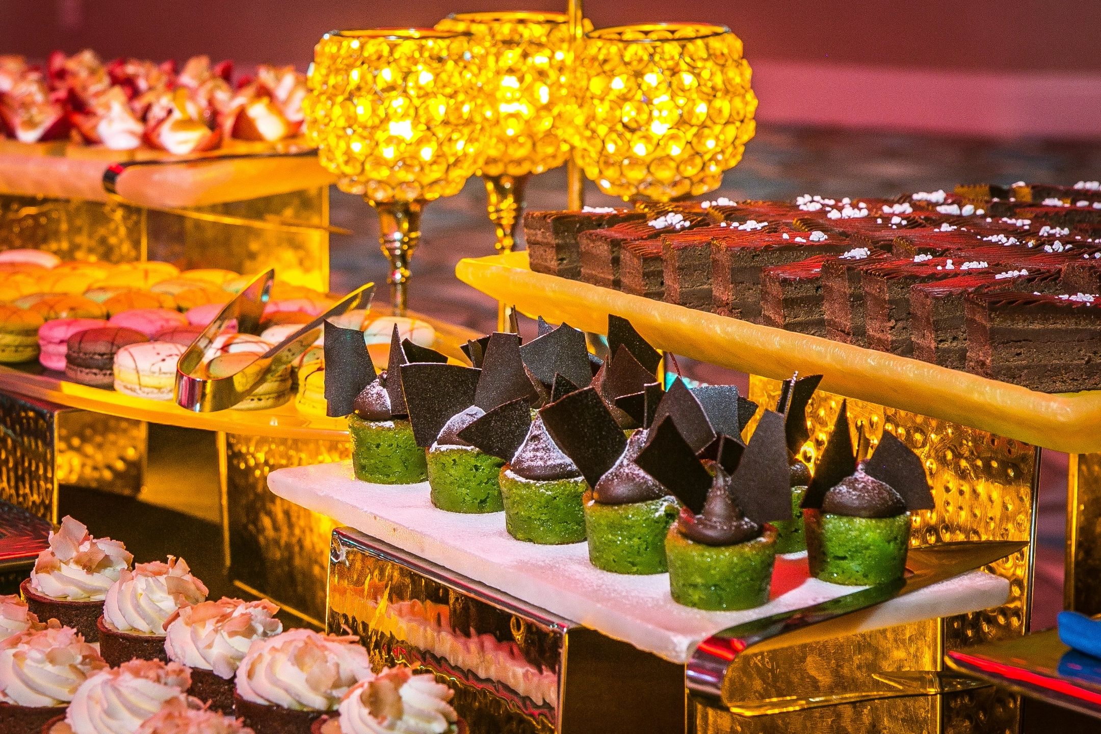 Assorted elegant desserts displayed on golden trays with warm lighting.