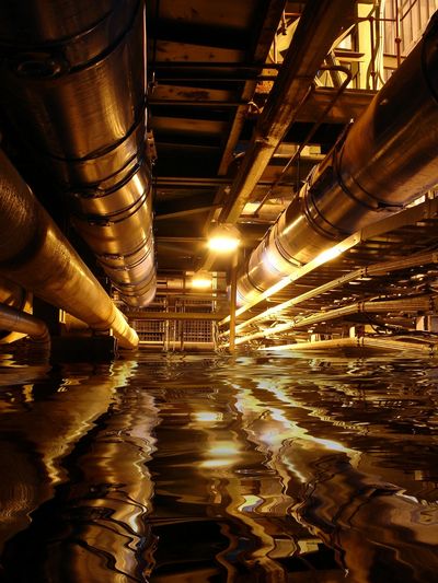 Industrial pipes above reflective water in a dimly lit setting.