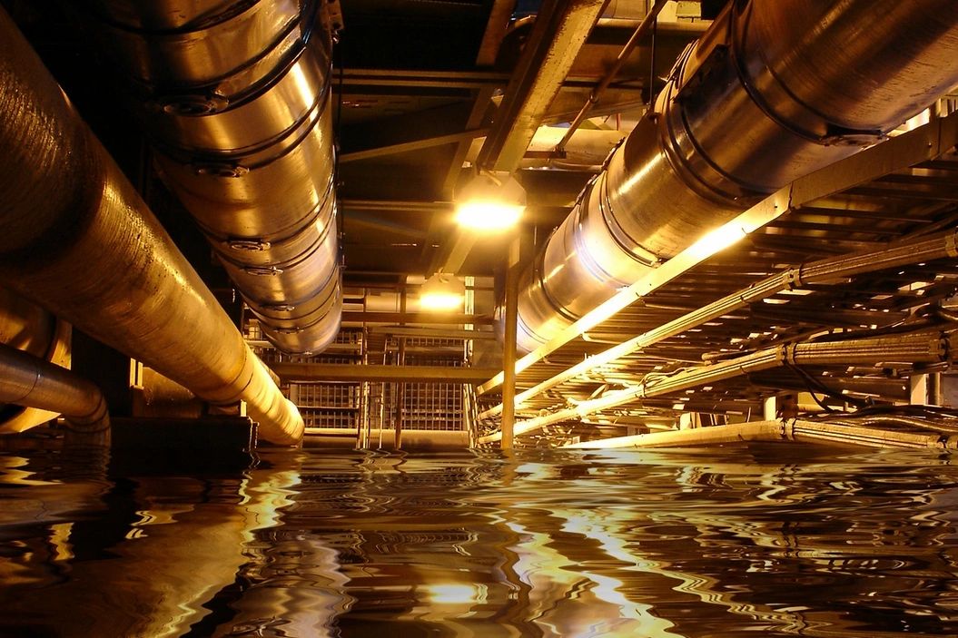 Industrial pipes reflecting on water in a dimly lit setting.