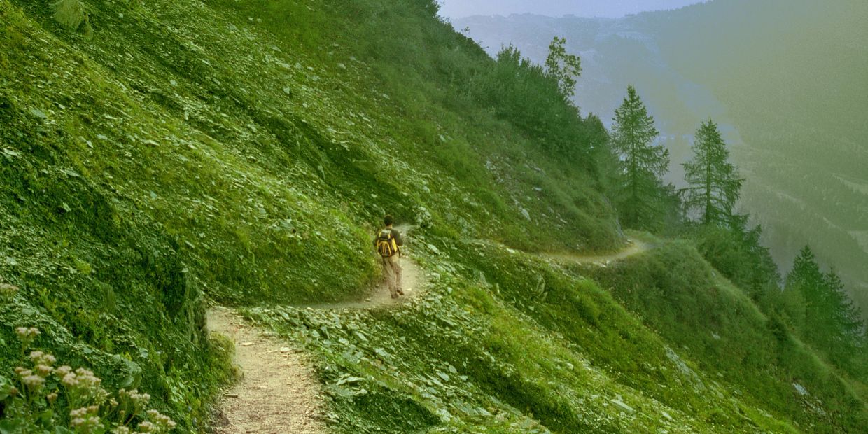 Person hiking on a narrow mountain trail.