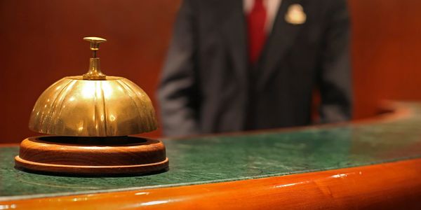 A vintage hotel reception bell on a green counter with a concierge in background.