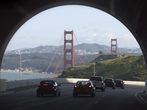 View of Golden Gate Bridge framed by tunnel with cars driving.