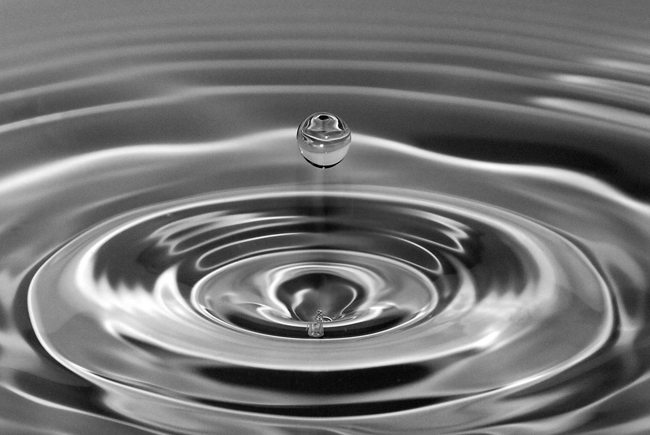 A droplet bounces above, as the waves created by the pressure, shows ripples spreading.