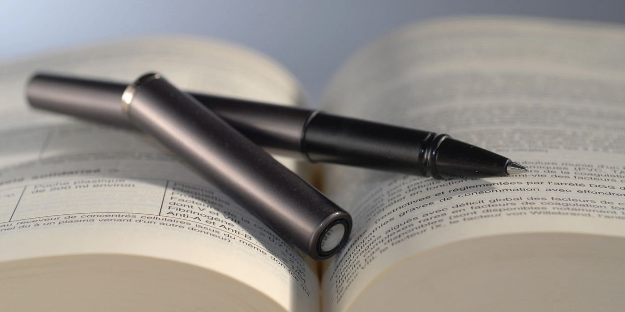 A fine-tipped black pen rests on an open text book.